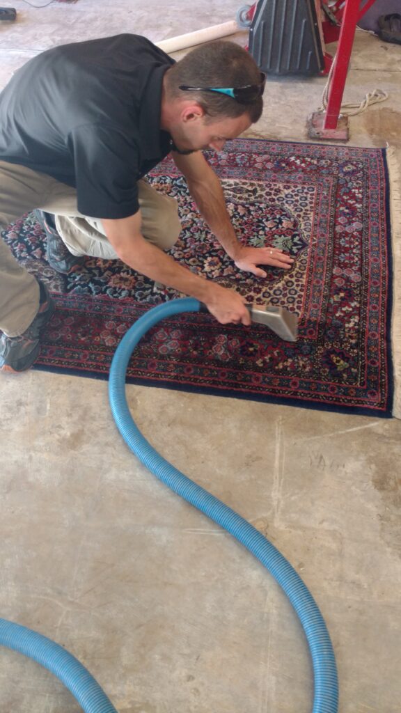 A man is vacuuming the area rug.